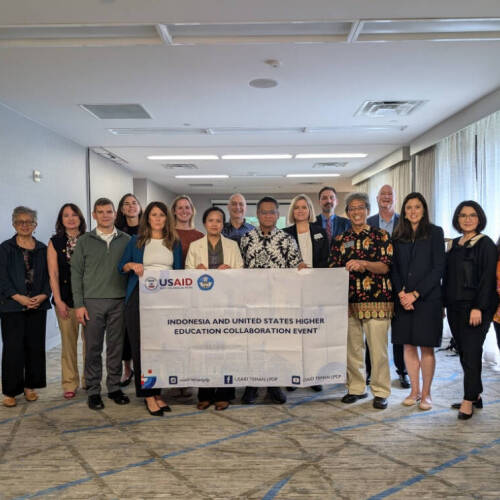A group of people stands together in a conference room holding a banner that reads "Indonesia and United States Higher Education Collaboration Event," with USAID and other partner logos, representing a formal gathering.
